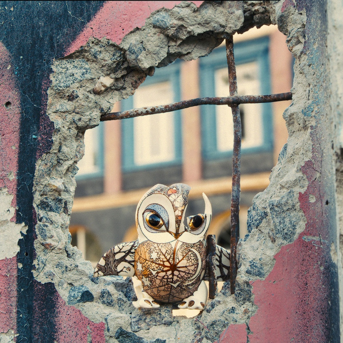 A porcelain owl peeking out of a hole in a wall.