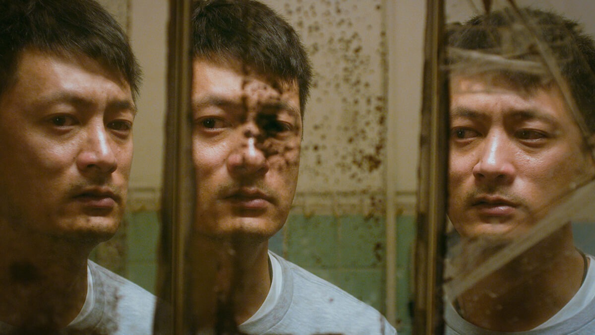 A man stares at himself in a rusted, shattered mirror that is reflected in three different angles.