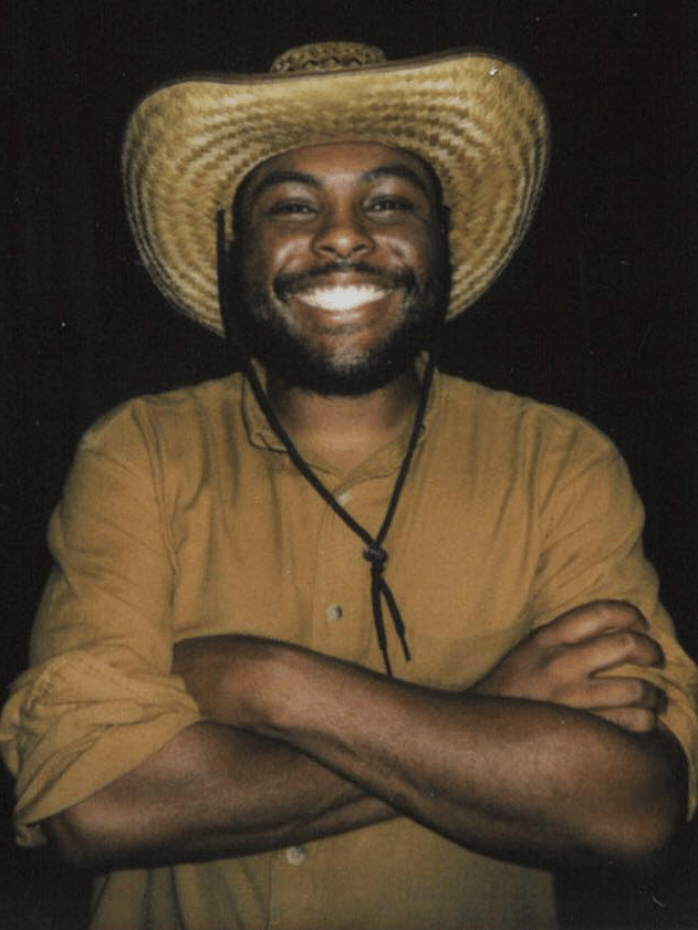 person with arms crossed wearing a cowboy hat smiling