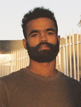 person with dark hair and beard outside
