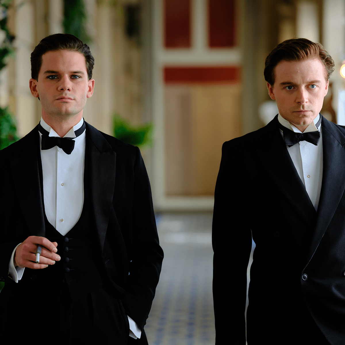 Two people in suits with bowties walking down a hallway