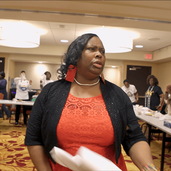 Person with papers in hand in a room of people on red and yellow carpet