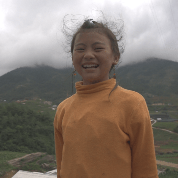 a child whose hair is being blown by the wind stands in front of mountains