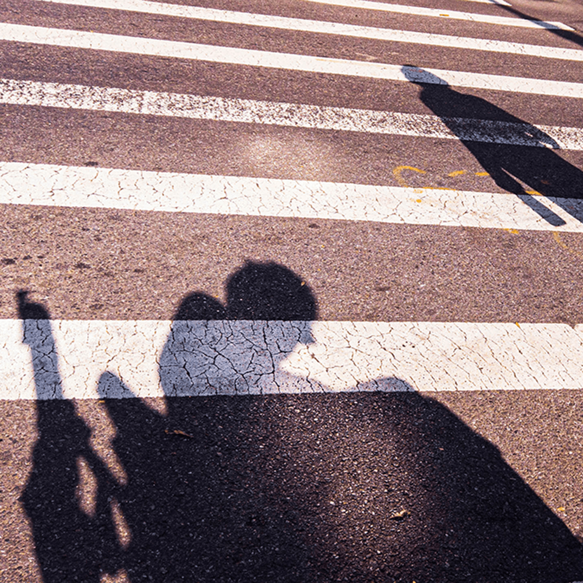 a person walking in a crosswalk next to a shadow of a person in wheelchair