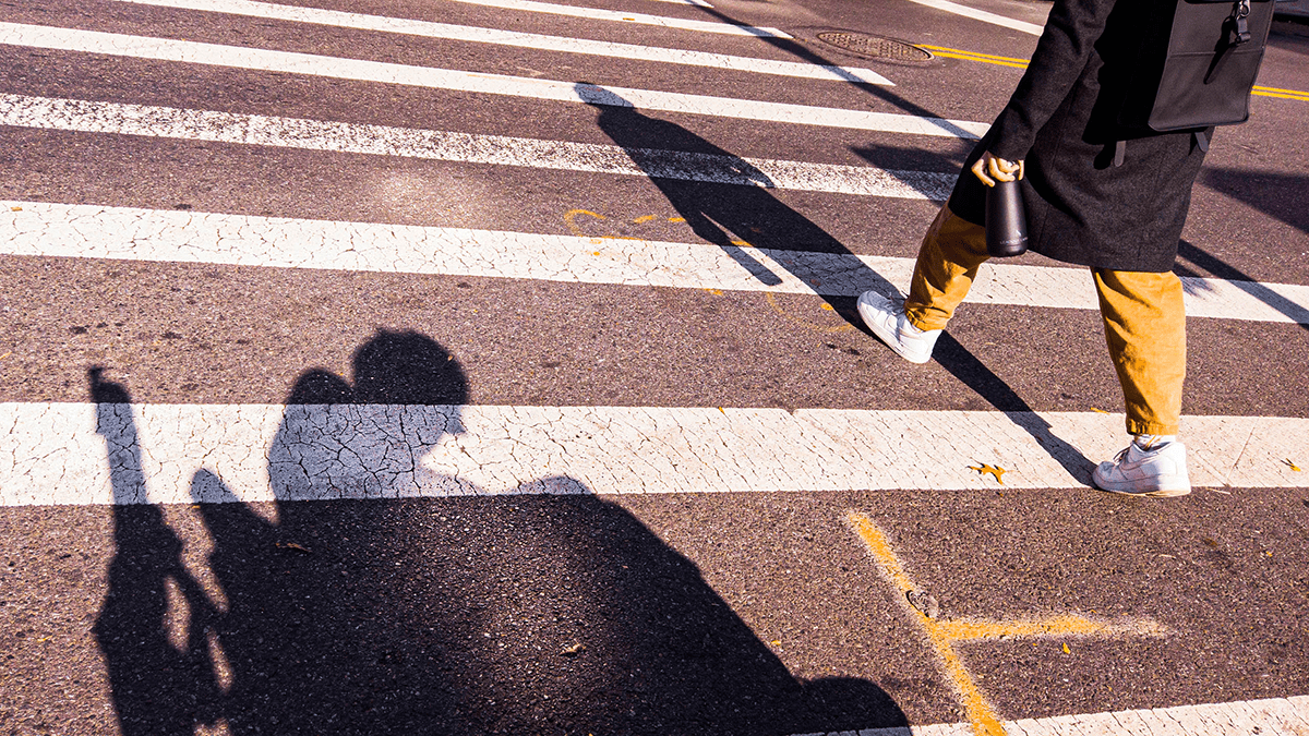 a person walking in a crosswalk next to a shadow of a person in wheelchair