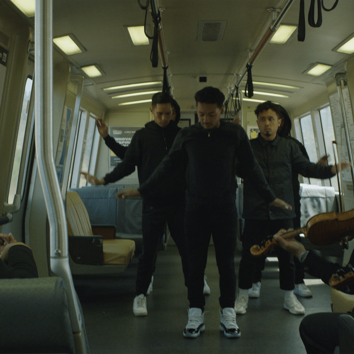 three people dance on a train filled with commuters