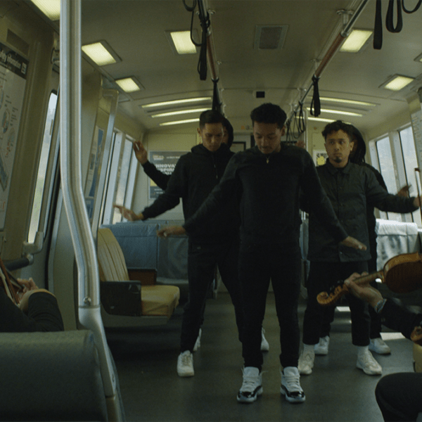 three people dance on a train filled with commuters