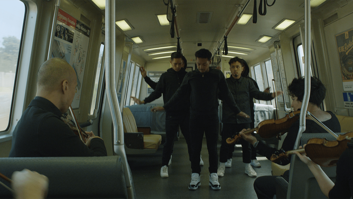 three people dance on a train filled with commuters