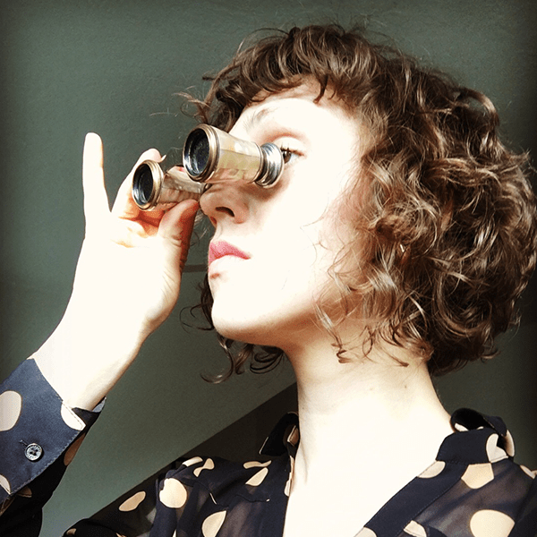 person with curly hair looking through gold binoculars