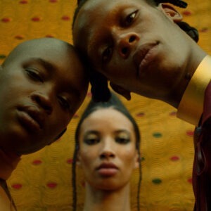 a group of three people stand together against a yellow patterned backdrop.