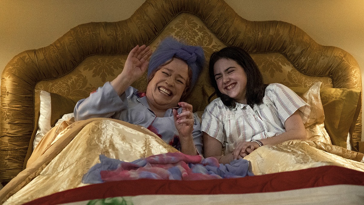 a woman and a young girl lay in bed together laughing.