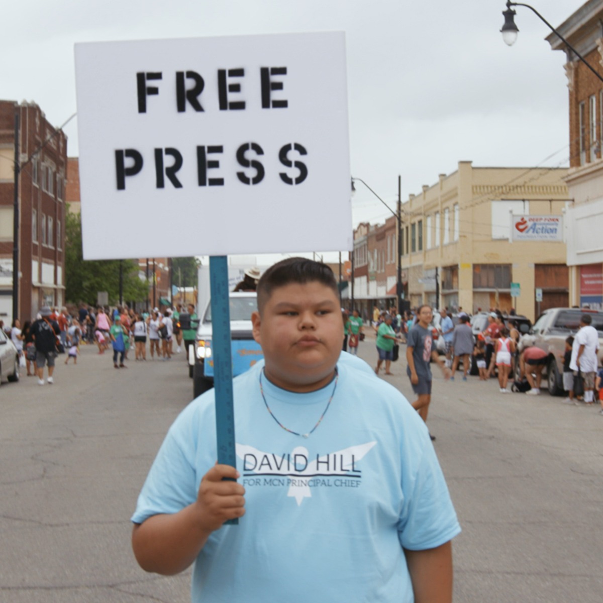 a young boy holding a sign that reads, "FREE PRESS" walking along a street.