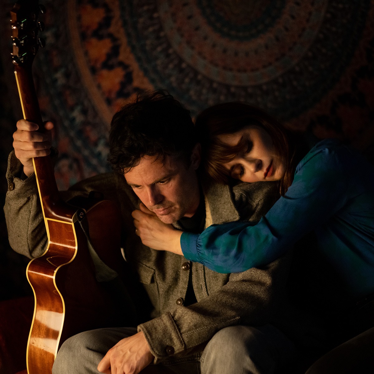a woman leaning on the shoulder of a man holding a guitar sit on a couch.