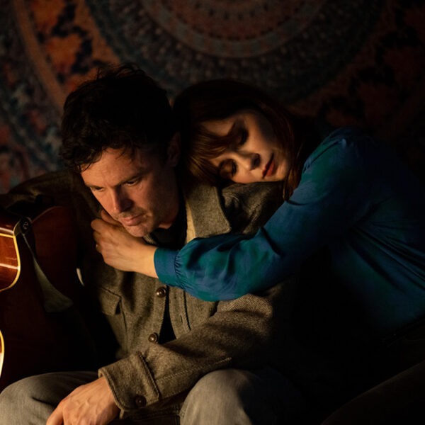 a woman leaning on the shoulder of a man holding a guitar sit on a couch.