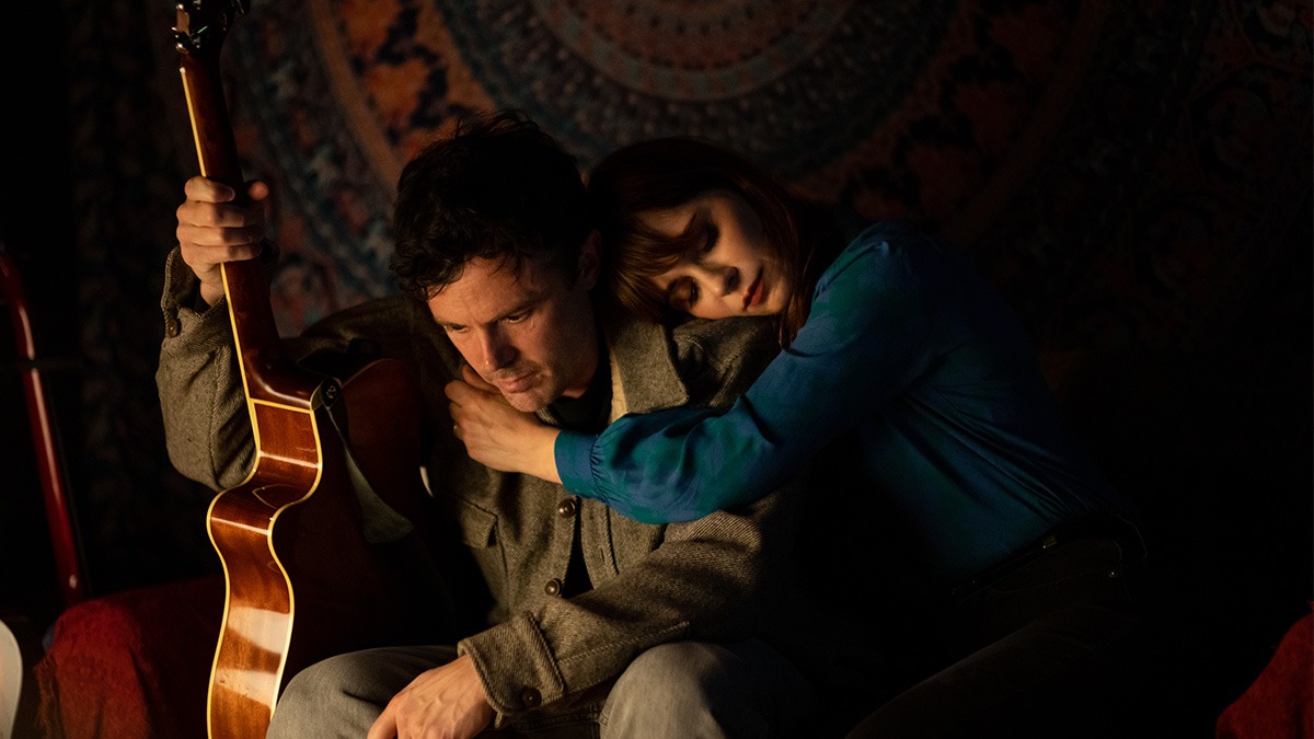 a woman leaning on the shoulder of a man holding a guitar sit on a couch.