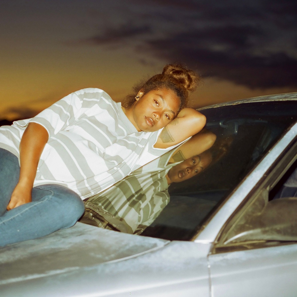 a woman sitting on a car hood at sunset.