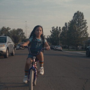 a young girl riding a purple bike through a neighborhood street.