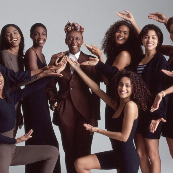 a group of smiling women pose around a woman wearing a brown suit.