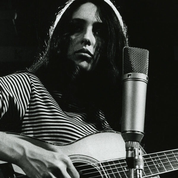a woman in a striped shirt playing guitar by a microphone.