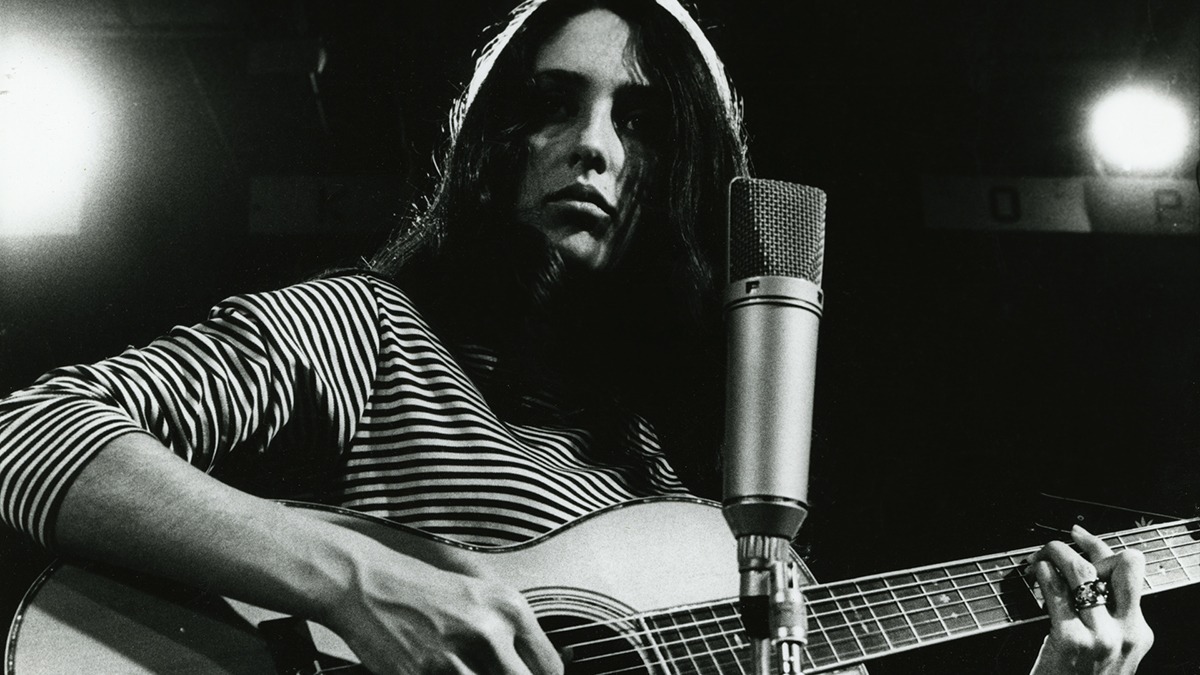 a woman in a striped shirt playing guitar by a microphone.