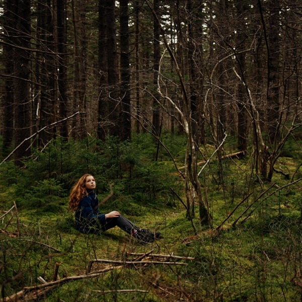 a girl sitting on the ground in a forest.
