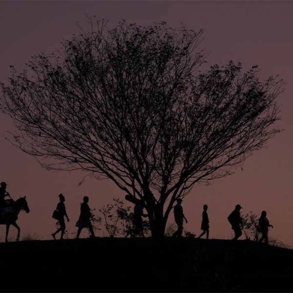 a group of naked woman stand by a wooden hut in a forest.
