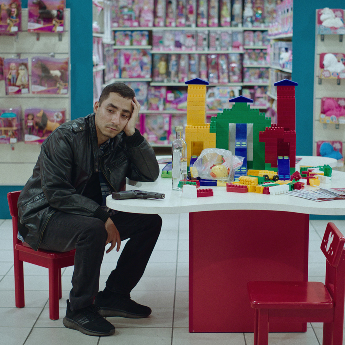 a man sits in a toy store with a gun and a lego building.