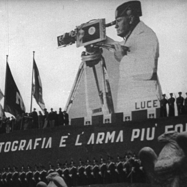 a large cutout of a man holding a camera stands over a crowd of soldiers.