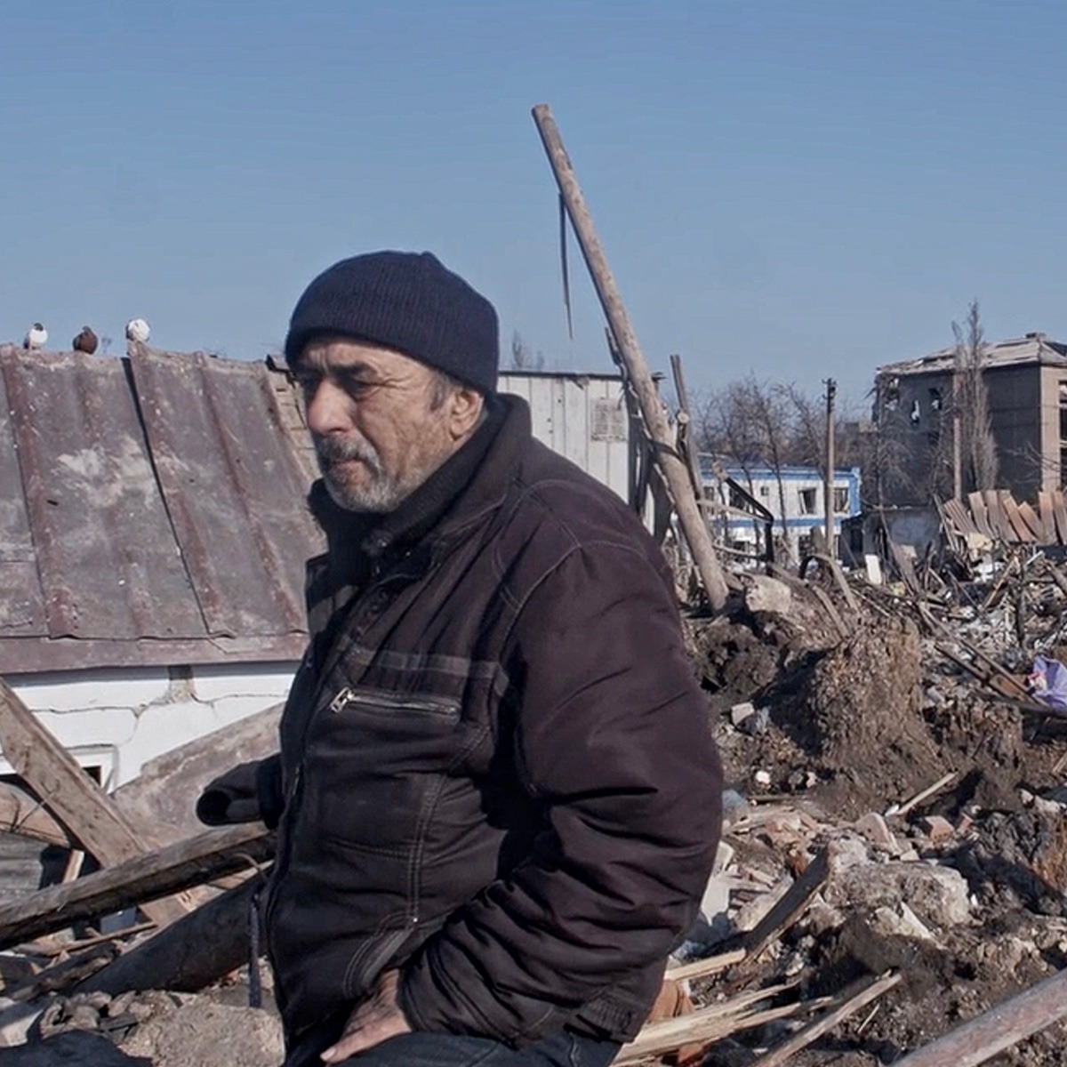 a man standing in front of a pile of rubble and destroyed buildings.
