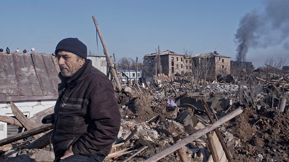 a man standing in front of a pile of rubble and destroyed buildings.