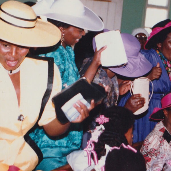 a group of women in fancy hats and dresses stand in the pews dancing and cheering.