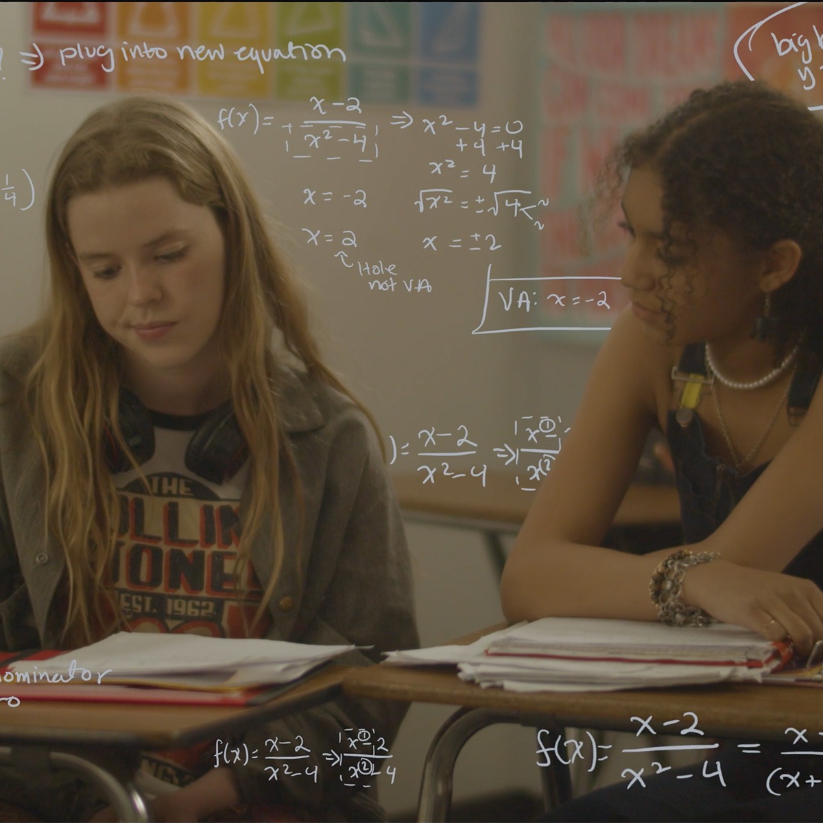 two schoolgirls sit at their desks with drawn equations surrounding them.