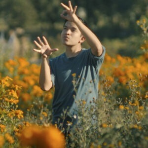 a man with his hands in the air standing in a field of yellow flowers.