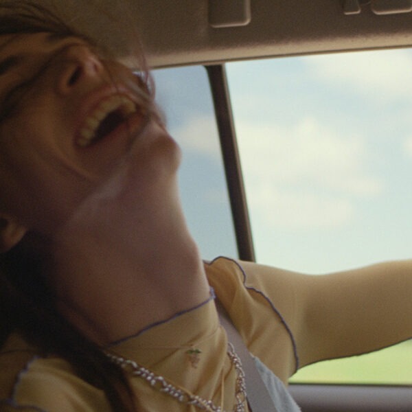 a young woman laughing in a car with her arm out the window.