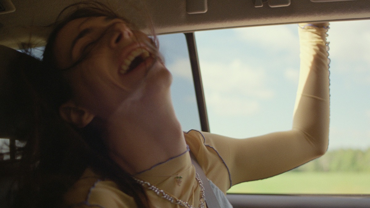 a young woman laughing in a car with her arm out the window.