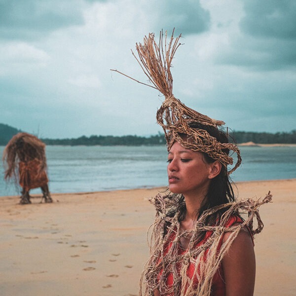 a woman with a straw headdress standing on a beach.