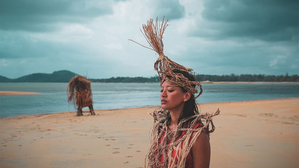 a woman with a straw headdress standing on a beach.