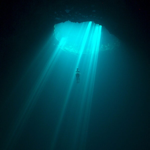 a woman underwater swimming up to a hole that has light shining through.
