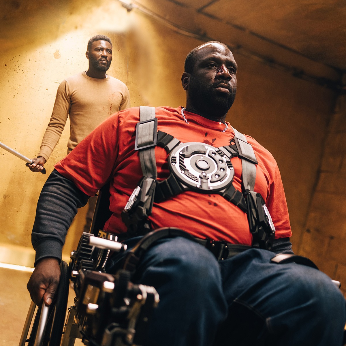 a man in a wheelchair followed by a man holding a club.