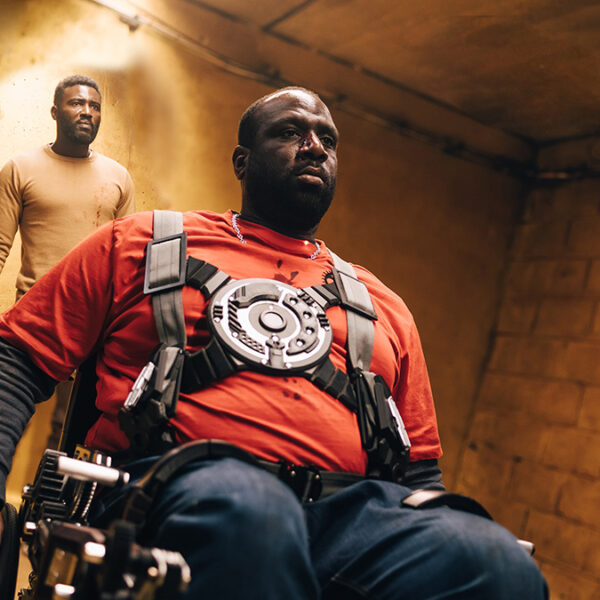 a man in a wheelchair followed by a man holding a club.