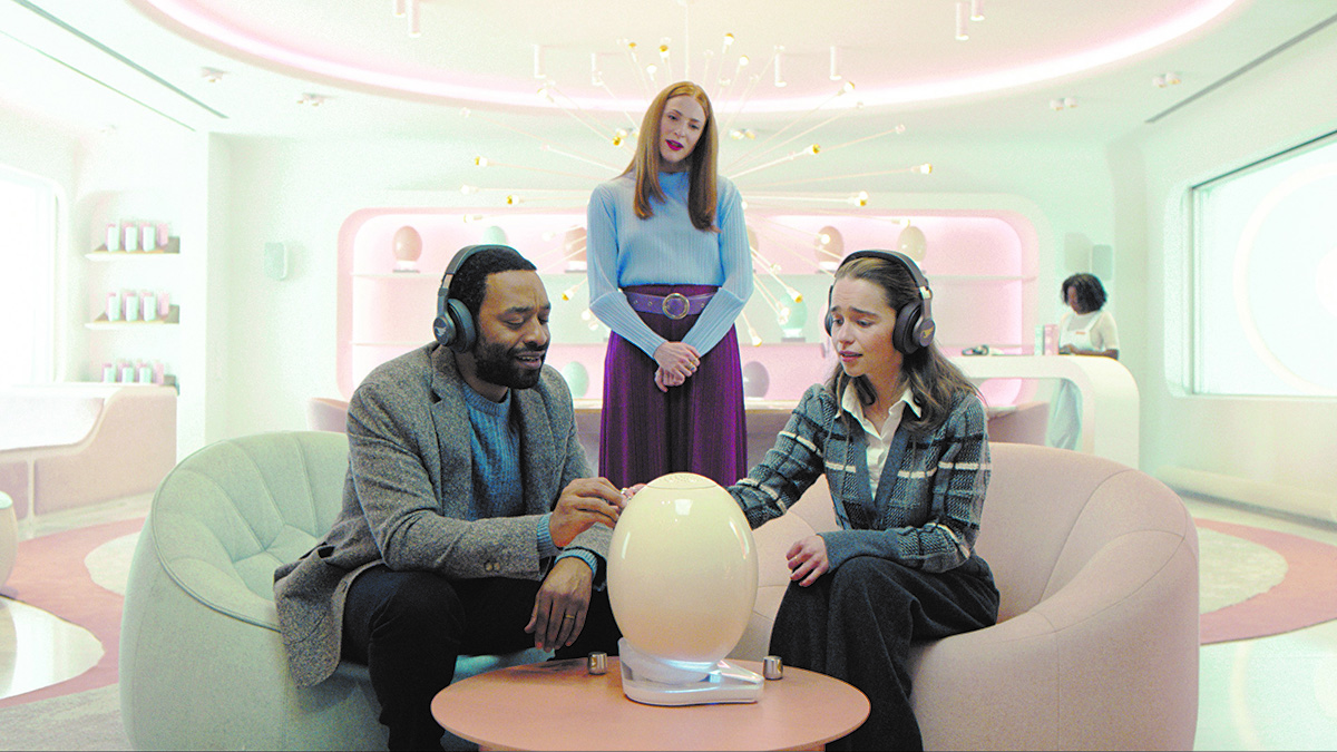 a man and a woman wearing headphones sitting next to a white pod in a futuristic room.