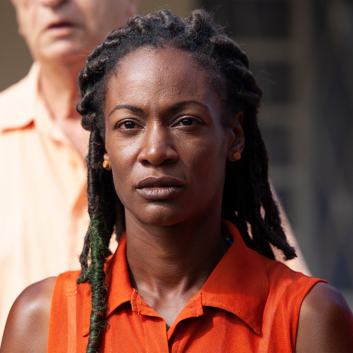 a woman with black hair in an orange shirt standing in front of a man.