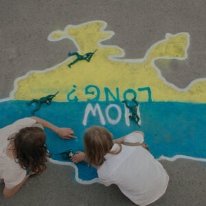 two young girls on a pavement drawing in chalk a map of Ukraine in the flag's colors with the words "how long?" written over it.