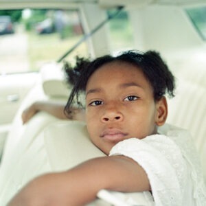 a young black child sitting in the back of an all white leather car interior.