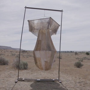 a fabric sculpture of an atomic bomb hanging on a frame in the desert.