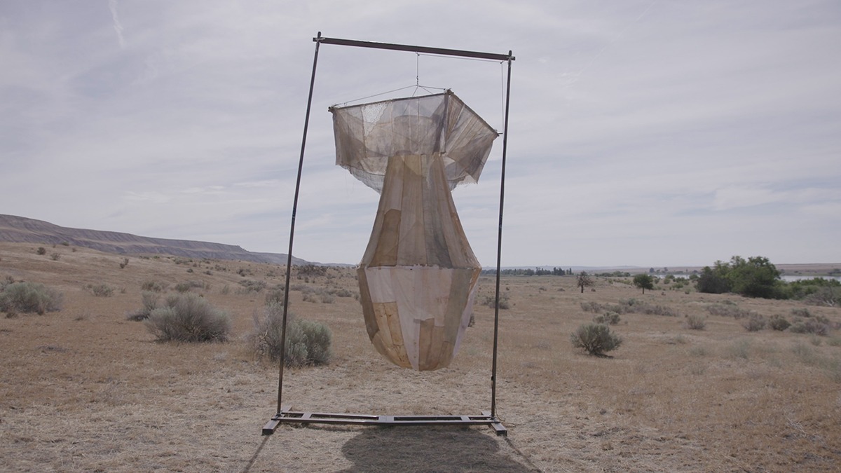 a fabric sculpture of an atomic bomb hanging on a frame in the desert.