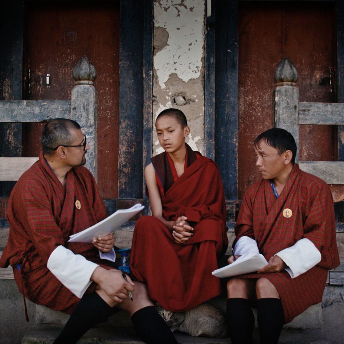 Three monks sitting outside a building.
