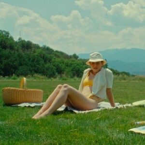 A woman with a hat lying on a blanket in a grassy field.