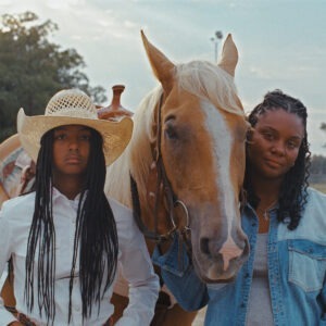 A girl in a cowboy hat standing next to a horse and another woman.