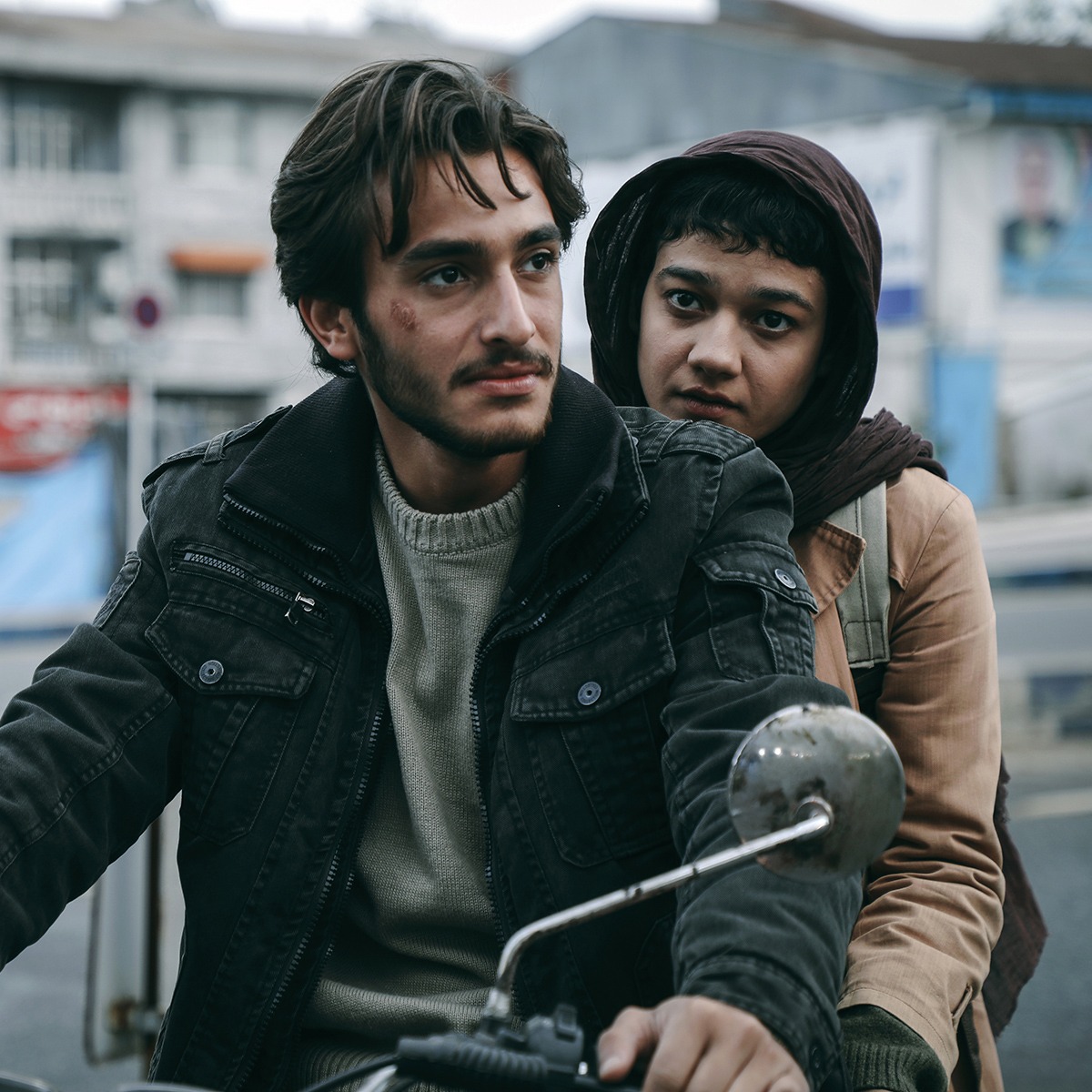A man and a woman sitting on a motorcycle in a city.